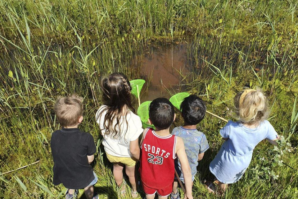 Vijf kinderen vissen met een visnetje in een vijver.