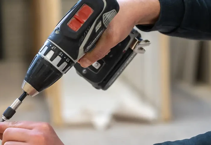 Hand houdt schroef vast. De andere hand schroeft de schroef in het hout met een electrische schroefmachine.