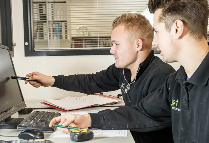 Twee mensen werken aan een computerscherm. Een van hen wijst iets aan op het scherm.